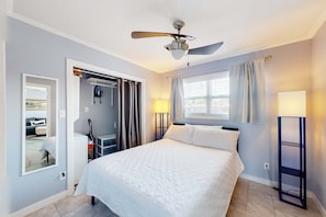 Ein Hotelzimmer mit Bett, Deckenventilator, Fenster mit Vorhängen, Nachttischlampe und Blick ins Freie.