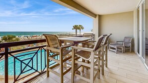 Un balcon avec une piscine, des meubles en bois et une vue sur la plage et l’océan.