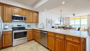 A modern kitchen with wooden cabinets, stainless steel appliances, and a large island. - Gulf Front 4BR | Pools | Hot Tub | Balcony | W/D (Fort Walton Beach)
