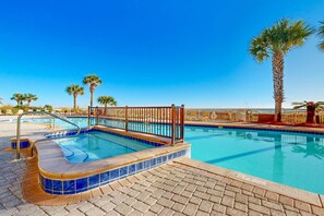 Una piscina con hidromasaje, rodeada de palmeras y sillones de descanso.