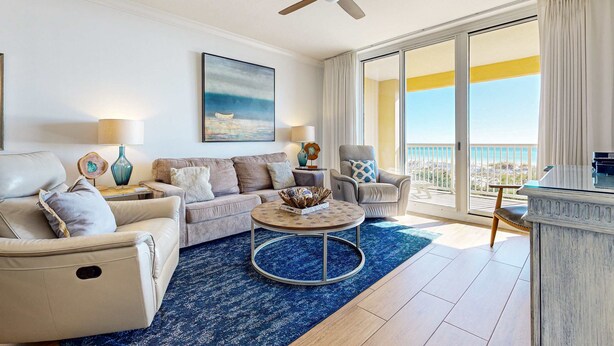 A spacious living room with a round coffee table, two sofas, a ceiling fan, and a large window with a view of the ocean. - Gulf Front 4BR | Pools | Hot Tub | Balcony | W/D (Fort Walton Beach)
