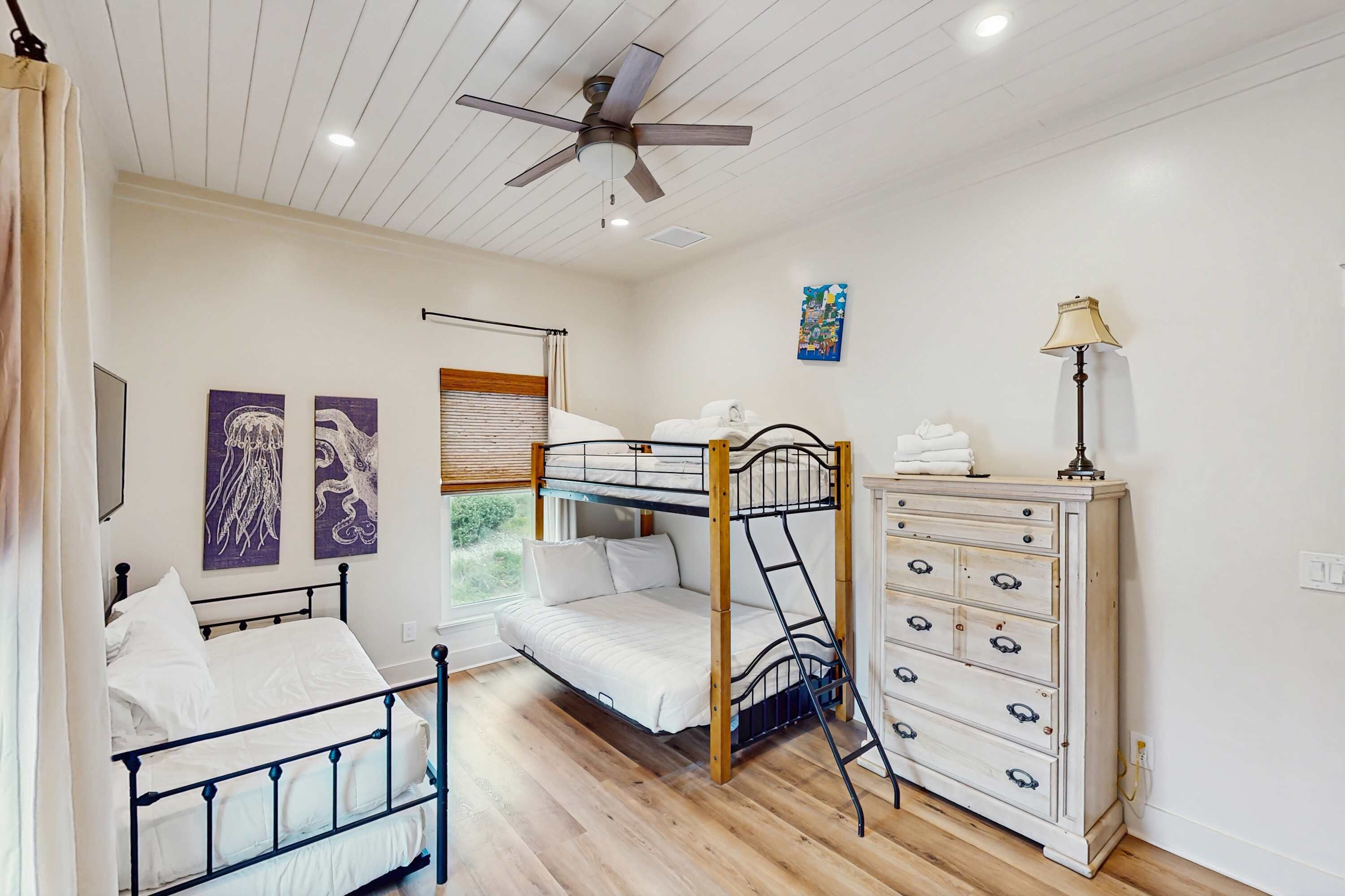 A bedroom with a bunk bed, a dresser, a ceiling fan, and artwork on the walls.