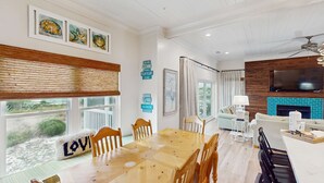 A spacious living room with a large wooden dining table, comfortable seating, a fireplace, and artwork on the walls. - Spacious home with private pool & full kitchen, close to beach (St. George Island)