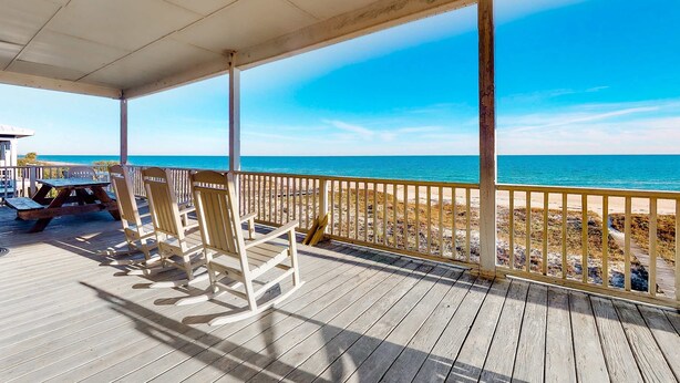 A wooden deck with chairs and a picnic table overlooking a beach. - Beachfront dog-friendly home with private hot tub, boardwalk, on-site pools, gym (St. George Island)