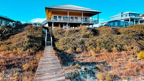 A coastal house with a wooden deck leading to a balcony. - Beachfront dog-friendly home with private hot tub, boardwalk, on-site pools, gym (St. George Island)