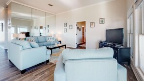 A modern living room with a light blue sofa, a coffee table, and a flat-screen TV on a black stand. - Beachfront dog-friendly home with private hot tub, boardwalk, on-site pools, gym (St. George Island)