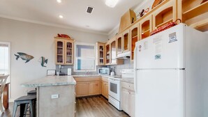A modern kitchen with wooden cabinets, a built-in oven, and a refrigerator. - Beachfront dog-friendly home with private hot tub, boardwalk, on-site pools, gym (St. George Island)