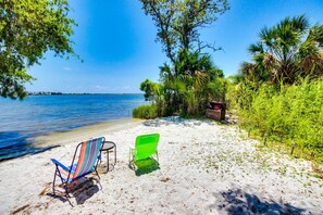 A beach with two beach chairs, a wooden bench, and a small table. - Cozy, waterfront studio condo with pool, dock & beach access (Fort Walton Beach)
