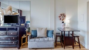 Ein modernes Wohnzimmer mit einem grauen Sofa, einem dunklen Holz-TV-Schrank und einem kleinen Tisch mit einer Lampe.