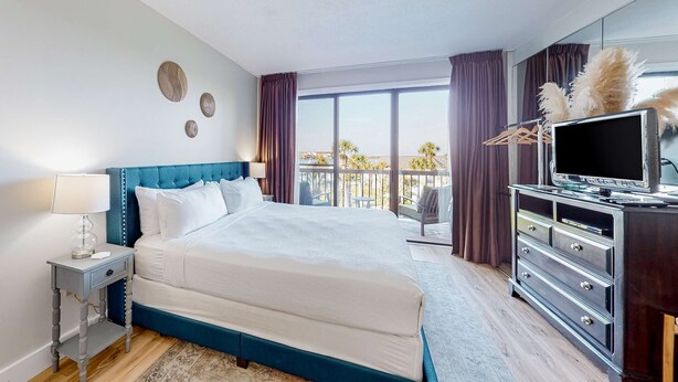 Ein Hotelzimmer mit einem großen Bett, einem Schminktisch, einem Fernseher und einem Balkon mit Blick.