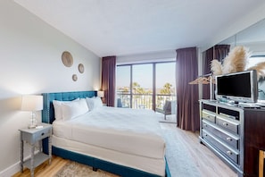 A hotel room with a large bed, a dresser, a TV, and a balcony with a view.