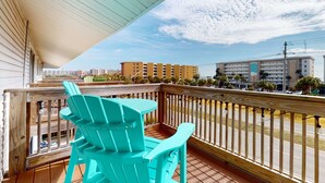Una terraza de madera con sillas Adirondack turquesas, barandilla y vistas a un paisaje urbano.