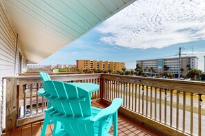 Een houten terras met turquoise Adirondack-stoelen, een leuning en uitzicht op een stadsbeeld.