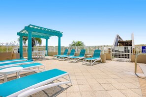 Ein Poolbereich auf dem Dach mit blauen und weißen Liegestühlen, einer Pergola und Blick aufs Meer.