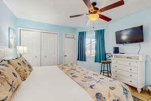 A bedroom with a bed, a ceiling fan, a TV, a dresser, and a window with curtains.