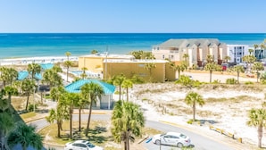 A coastal hotel with a beach view, a parking area, and palm trees. - Gorgeous coastal home with plenty of space and easy beach access (Fort Walton Beach)