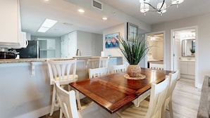 A modern kitchen with white cabinetry, a wooden dining table, and a chandelier. - Gorgeous coastal home with plenty of space and easy beach access (Fort Walton Beach)