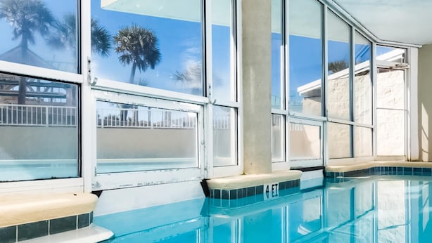 A clear indoor swimming pool with a view of palm trees and a building outside. - Gorgeous coastal home with plenty of space and easy beach access (Fort Walton Beach)