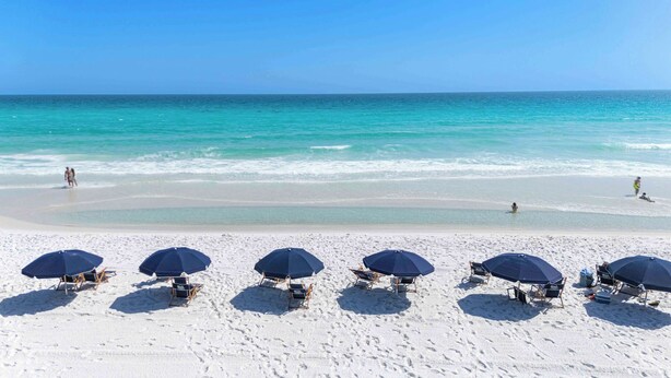 Una playa de arena blanca, agua turquesa cristalina y varias sombrillas.