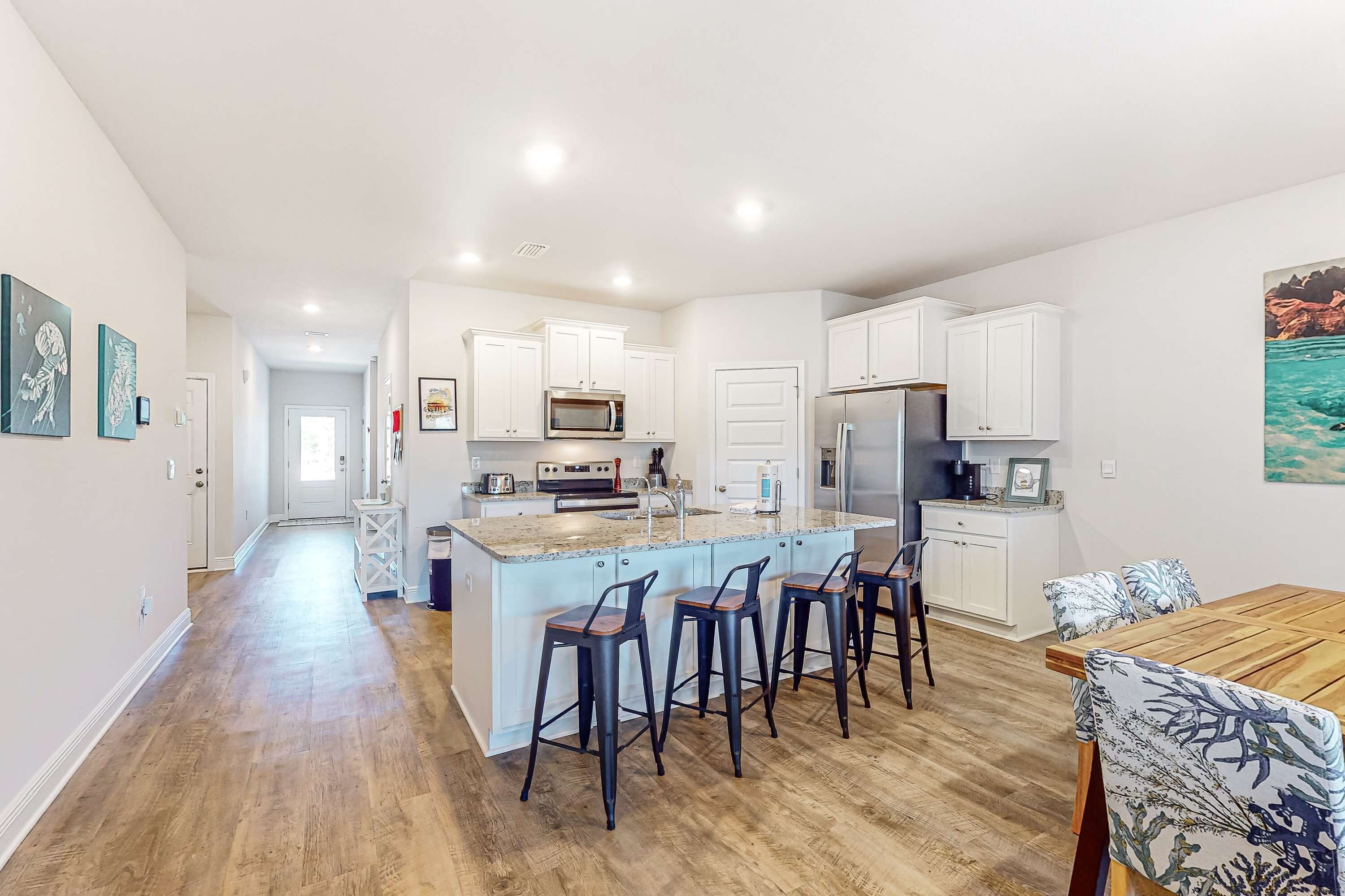 A modern kitchen with white cabinets, a central island with bar stools, and a dining area with a wooden table and chairs.