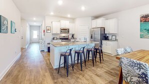 A modern kitchen with white cabinets, a central island with bar stools, and a dining area with a wooden table and chairs. - 2 dog-friendly beach homes with on-site pool, shopping, dining, AC, & WD (Port St. Joe)