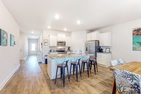 A modern kitchen with white cabinets, a central island with bar stools, and a dining area with a wooden table and chairs.