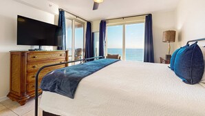 Un cuarto de hotel con cama, televisión, ventilador de techo, cómoda y vista al mar.