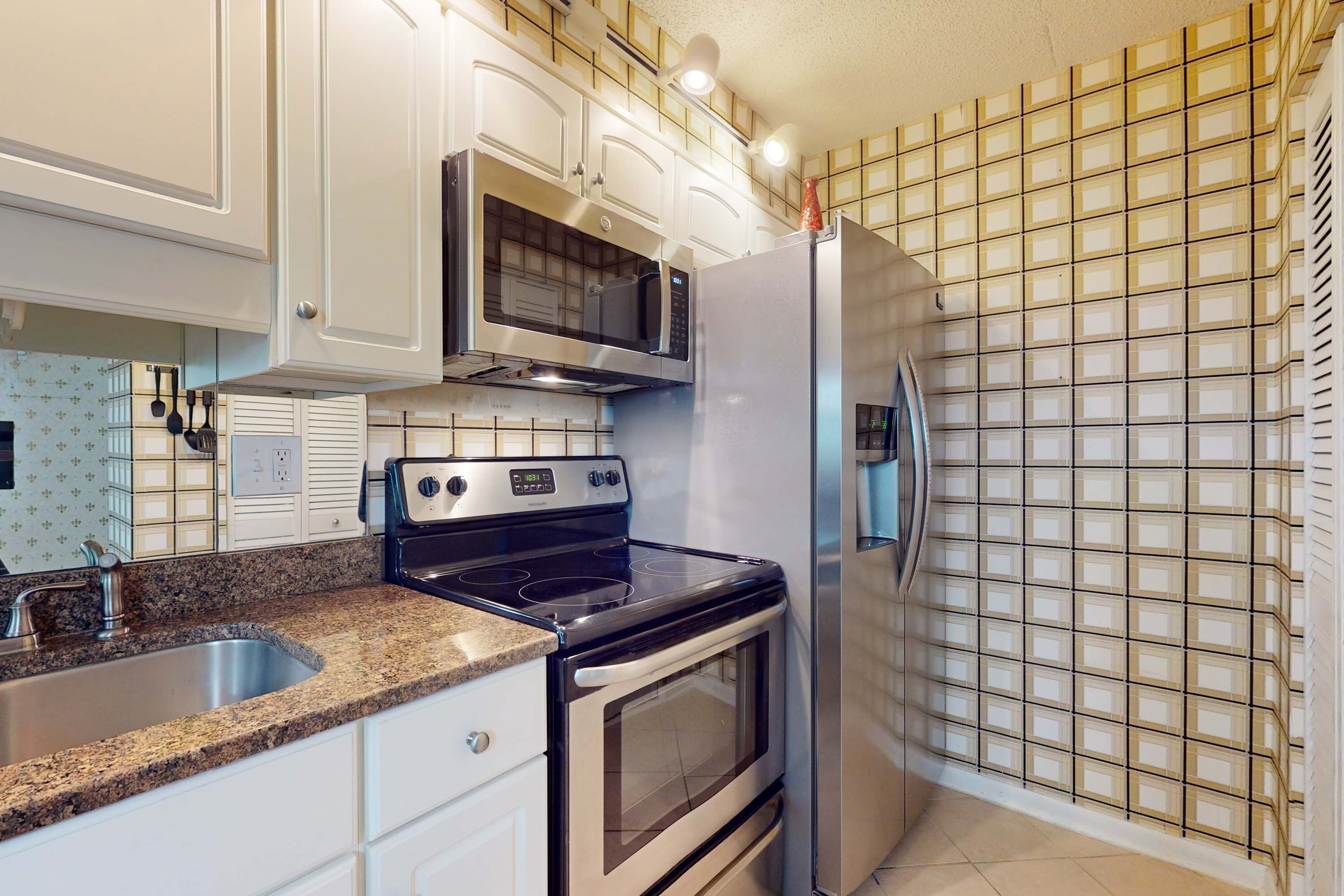 A kitchen with white cabinets, a stainless steel refrigerator, a microwave, a stove, and a tiled backsplash.
