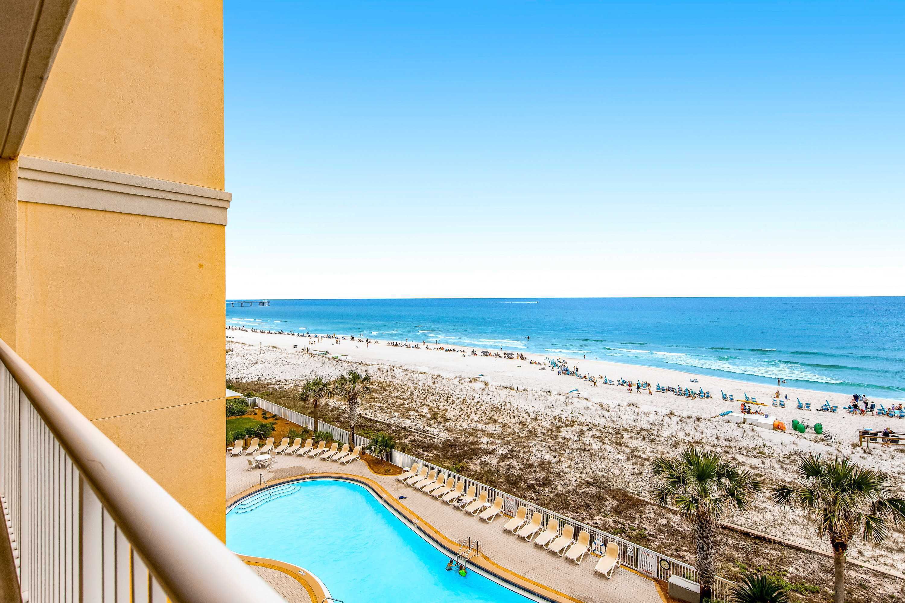 A poolside view with a beach and ocean in the background.