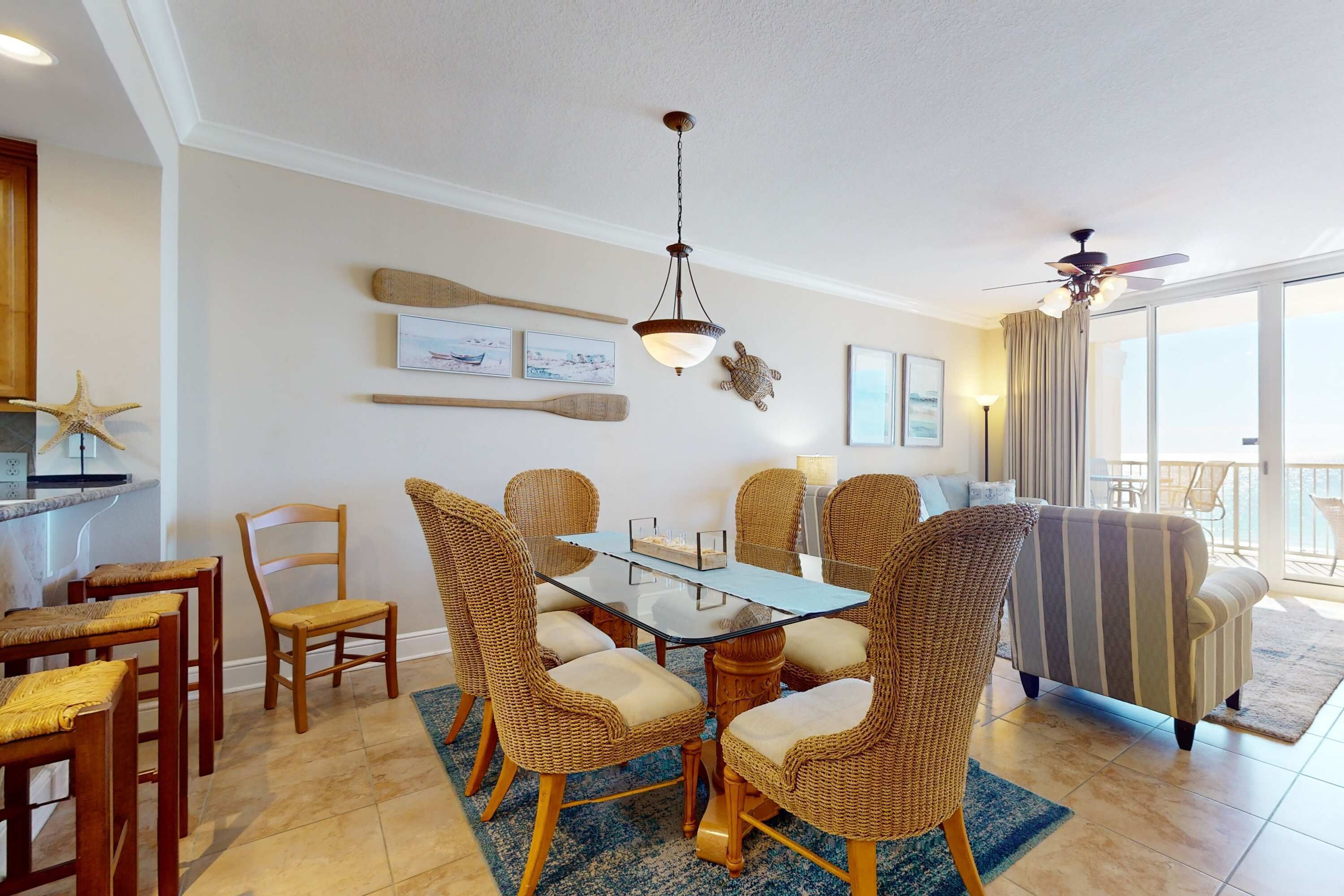 A dining area with wicker chairs, a glass table, and a ceiling fan.
