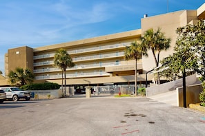 Ein mehrstöckiges Hotel mit Balkonen, Palmen und einem Parkplatz.