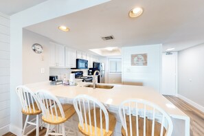 A modern kitchen with white cabinetry, a large island with bar stools, and built-in appliances. - Gulf-front condo with HD flat-screen televisions Tiki bar & Sky bar on-site (Miramar Beach)