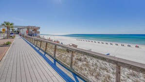 Ein hölzerner Steg führt zu einem Strand mit blauem Himmel und ruhigem Wasser.