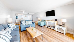 Ein modernes Wohnzimmer mit einem blauen Sofa, einem Holztisch und einem an der Wand befestigten Fernseher.