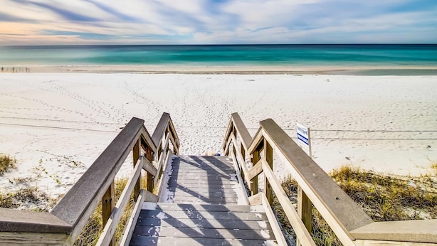 Een houten trap die naar een strand leidt, met een heldere lucht.