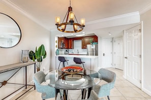 Un espace repas moderne avec une table en verre, quatre chaises, un vase décoratif et un lustre.