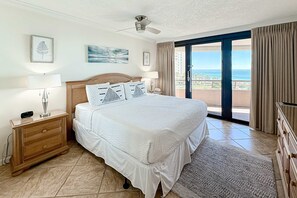 A hotel room with a large bed, a wooden nightstand, a ceiling fan, and a view of the ocean through a sliding glass door. - Gorgeous coastal condo with shared pool and easy beach access (Miramar Beach)