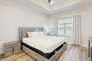 Una camera da letto con un letto con struttura in legno, biancheria da letto bianca, un comodino e una finestra con tende.