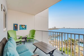 A balcony with a view of the sea, a green chair, a blue sofa, and two artworks on the wall. - 4th Floor Condo, On-Site Pool, Amazing View, Beach-Front (Pensacola Beach)