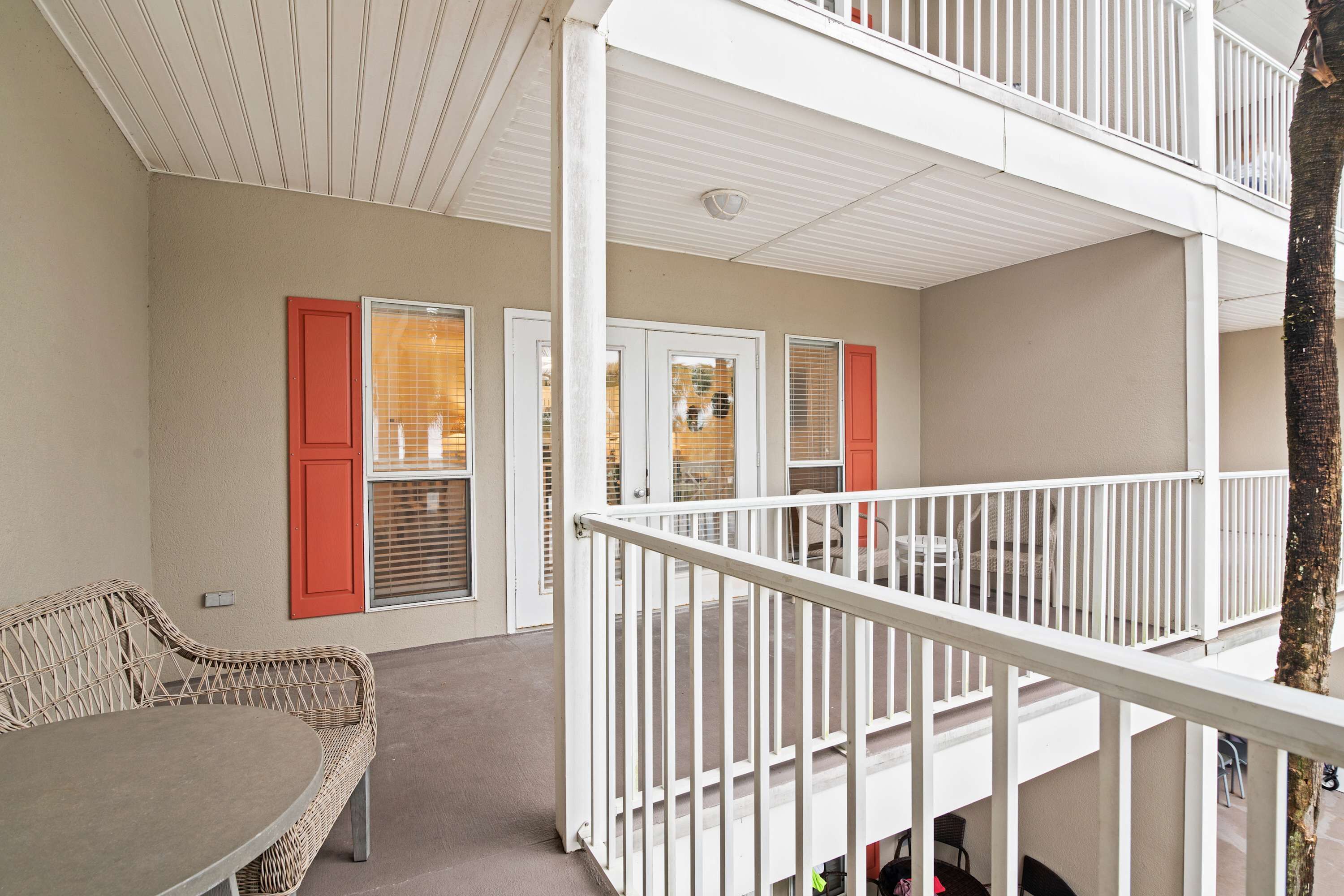 A multi-level balcony with white railings, a wicker sofa, and a table.