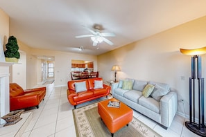 A living room with a red leather sofa, a grey sofa, and a coffee table. There is a ceiling fan, a lamp, and a TV stand.