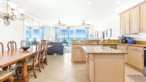 A modern kitchen with a central island, dining area with wooden chairs, and a view to the sea. - Gorgeous Gulf front townhome, Gas grill and beach access (Pensacola Beach)