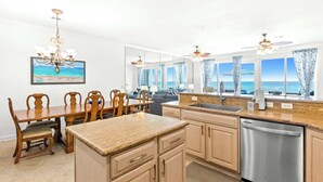 A modern kitchen with a view of the ocean, wooden dining table, and a stainless steel dishwasher. - Gorgeous Gulf front townhome, Gas grill and beach access (Pensacola Beach)