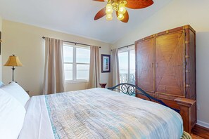 A bedroom with a large bed, a wooden wardrobe, a ceiling fan, and a window with curtains. - Bayview Condo with Shared Pool, Beach Nearby - Snowbirds Welcome (Pensacola Beach)