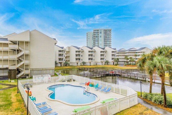 A hotel with a swimming pool, a dock, and a view of a tall building. - Bayview Condo with Shared Pool, Beach Nearby - Snowbirds Welcome (Pensacola Beach)