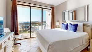 A hotel room with a large bed, a dresser, a TV, and a balcony with a view. - Bayfront delight with pool, bay views & prime location - snowbird-friendly (Fort Walton Beach)