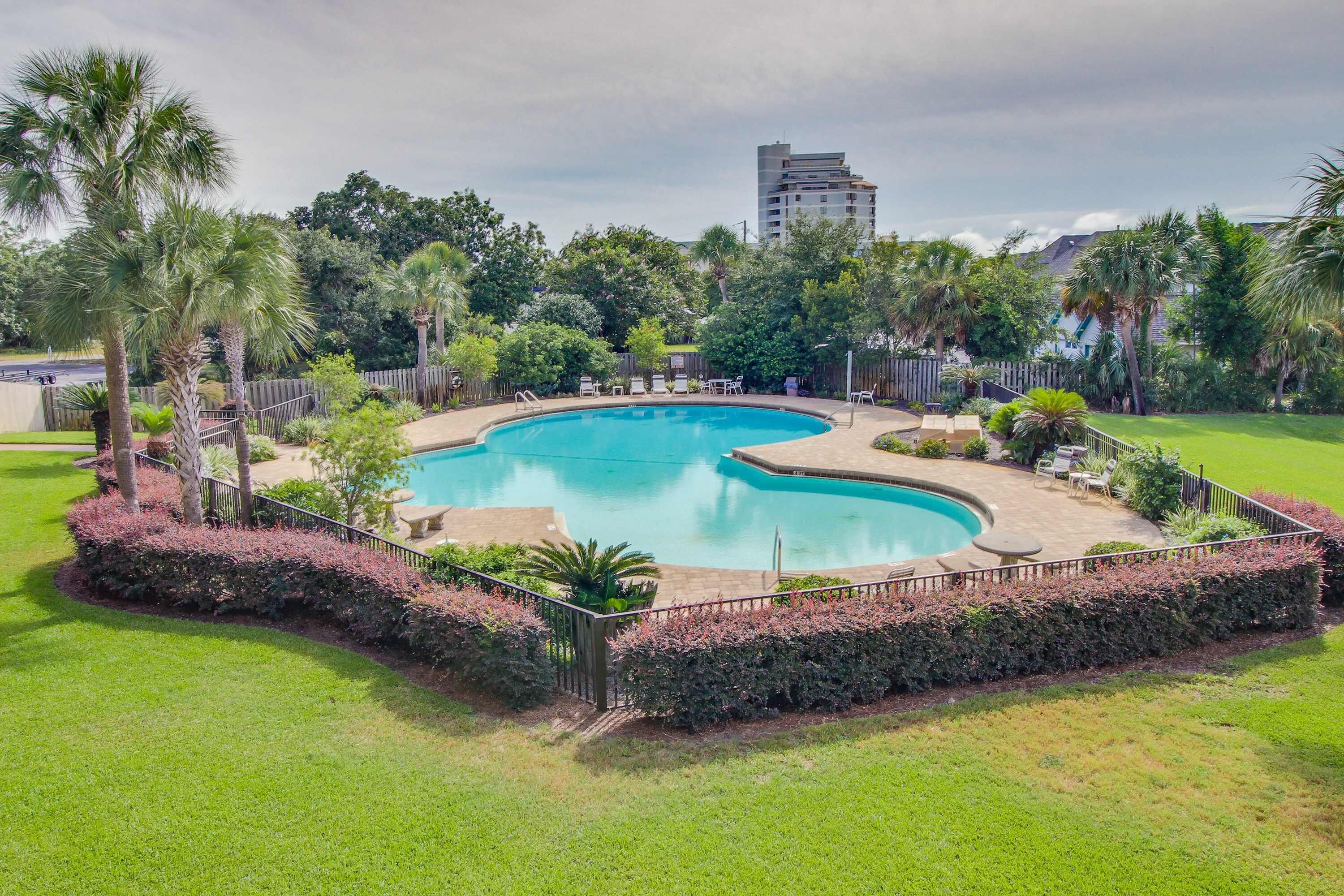 Piscina cercada por uma grade, com palmeiras e área gramada.