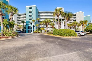 A hotel with multiple floors, a central entrance, and palm trees. - Destin West Bayside Pelican 608 - Gorgeous bayside condo with lazy river and beach access (Fort Walton Beach)