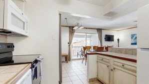 A kitchen with a microwave, stove, and cabinets, leading to a balcony with a table and chairs. - Cozy Coastal Gulf Condo with Shared Pool and Beach Access (Pensacola Beach)