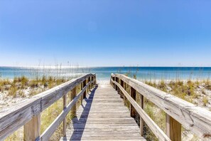 Ein Holzsteg führt zu einem Strand unter blauem Himmel.